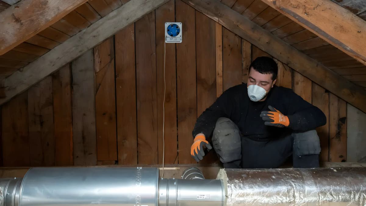 Tekniker med skyddsmask och handskar monterar galvaniserade ventilationskanaler med avstick på en vind i Stockholm